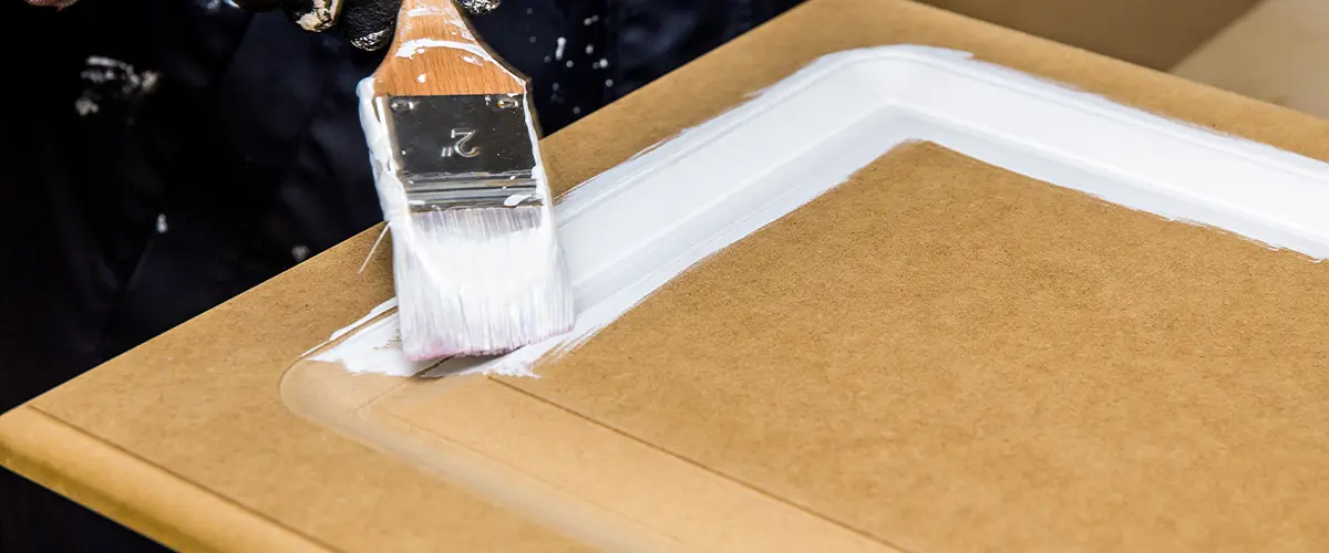 hand refinishing a cabinet with white paint